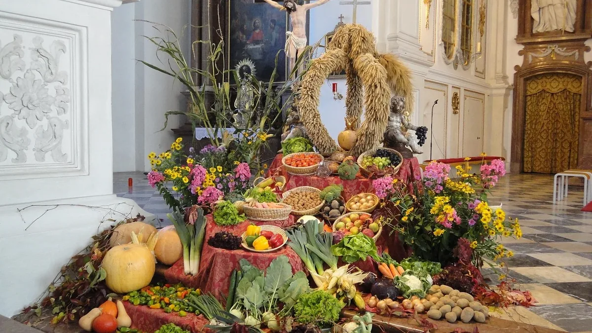 A large arrangement of fruits, vegetables, and flowers on a table in a church, with a crucifix in the background.