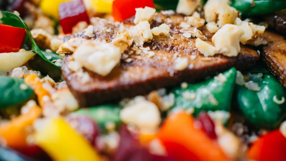 A close-up of a salad with a variety of ingredients, including vegetables, nuts, and possibly meat or tofu.