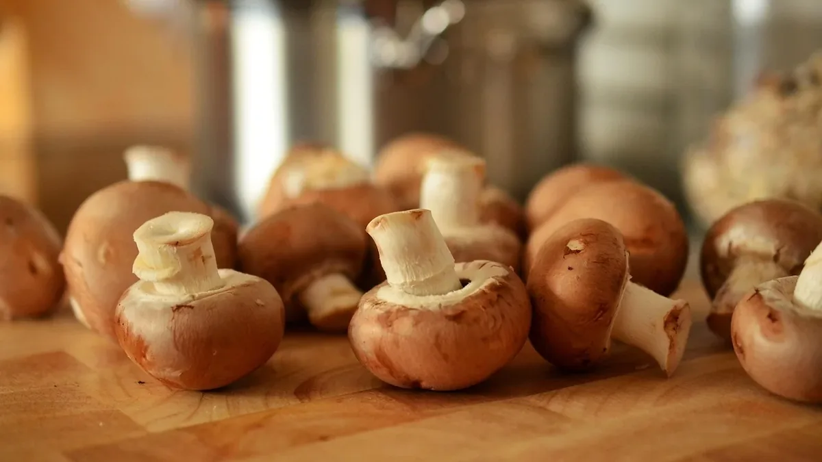 A collection of mushrooms on a wooden surface, with a stainless steel pot in the background.