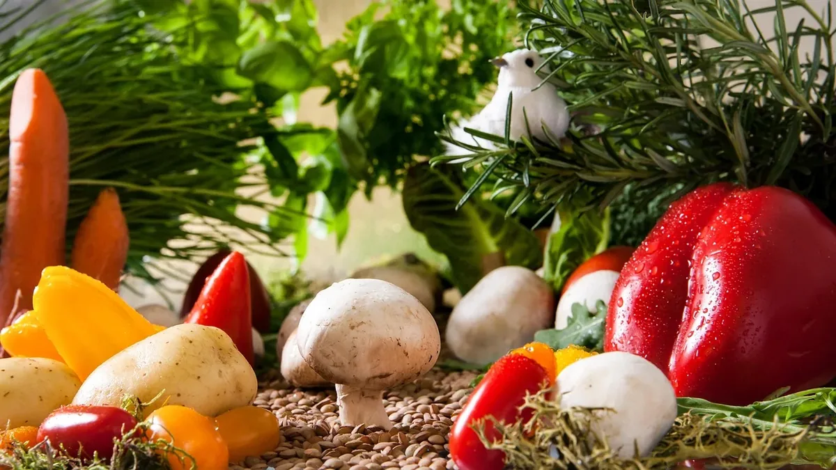 A diverse arrangement of vegetables, including carrots, mushrooms, peppers, potatoes, and herbs, set against a backdrop of a table or counte