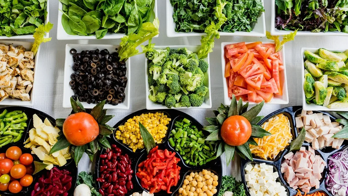 A table covered with various types of salad ingredients, including leafy greens, vegetables, fruits, and nuts.