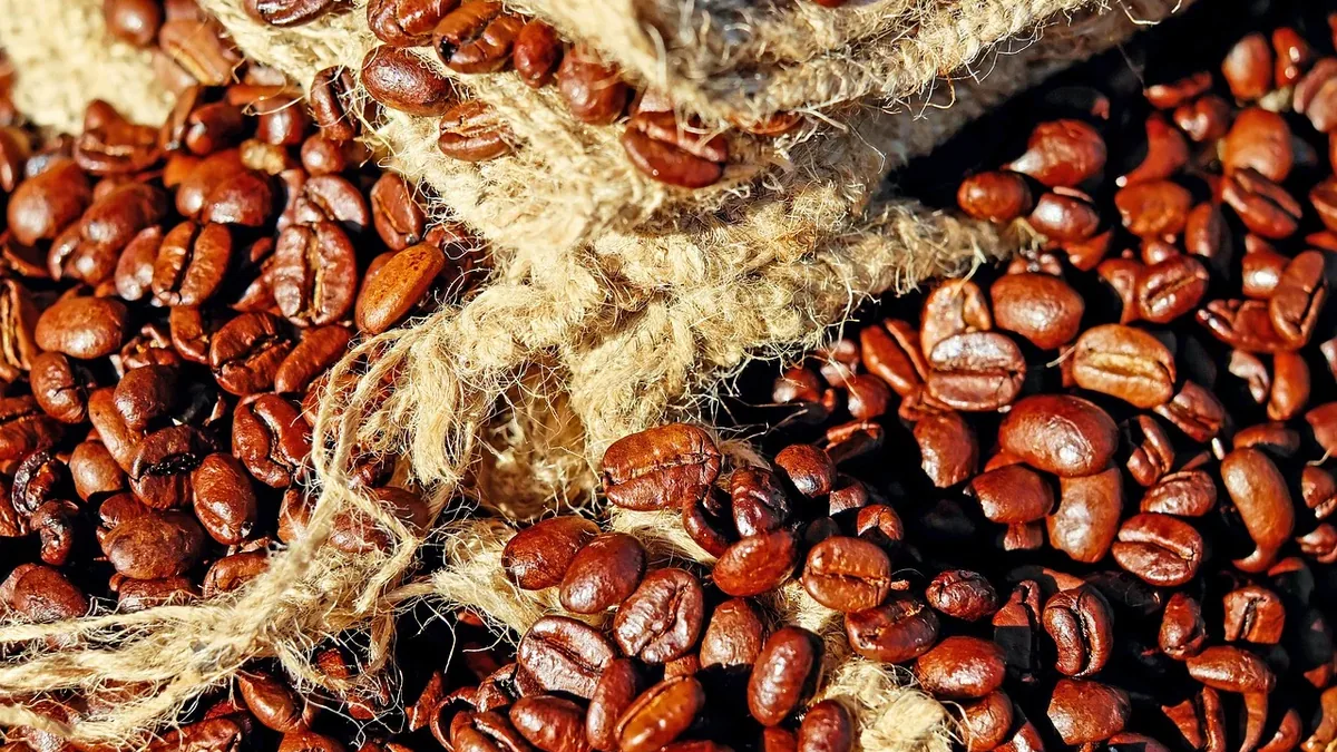 A close-up of roasted coffee beans spilling out of a burlap sack, with the beans scattered across the surface and the sack's twine visible i