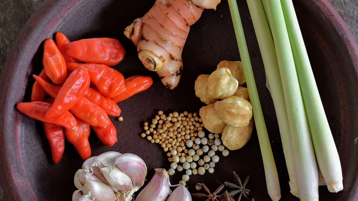 A collection of various spices and herbs arranged on a plate, including red chili peppers, ginger, lemongrass, garlic, star anise, and other