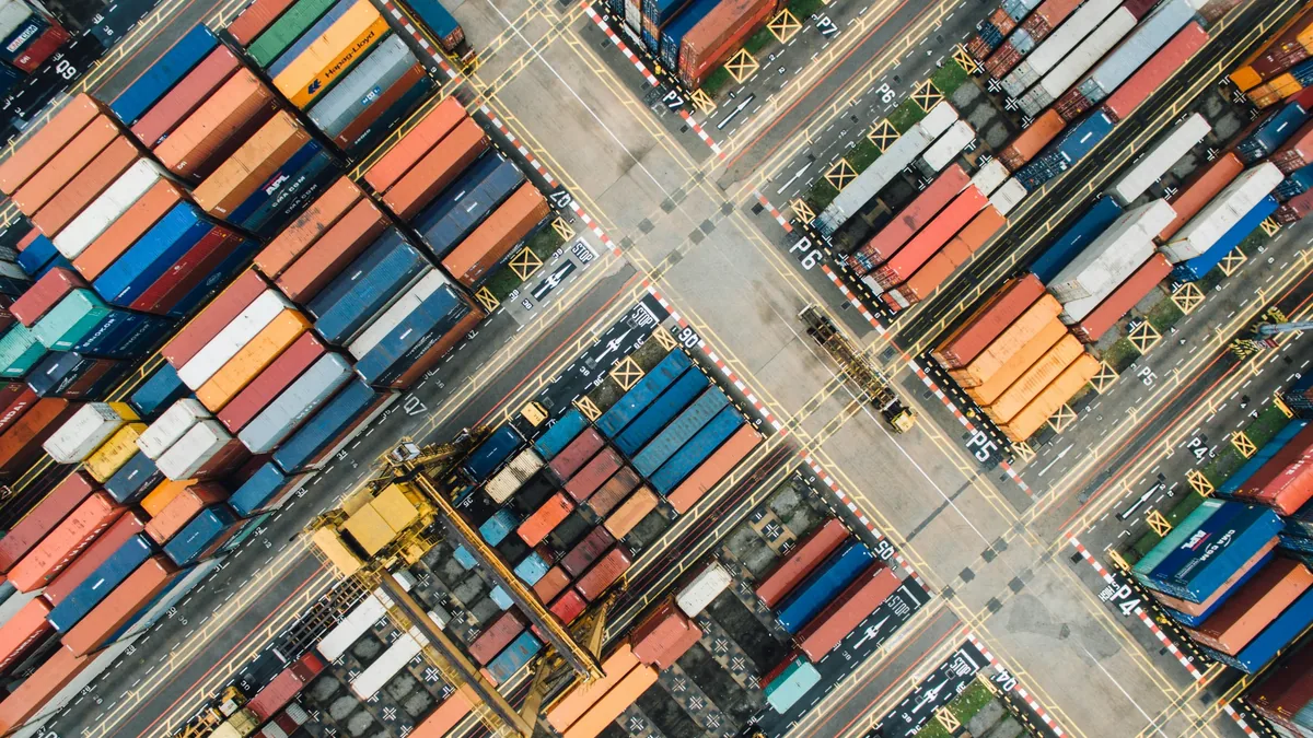 A large number of shipping containers stacked in rows, with some containers being transported by trucks or trains.