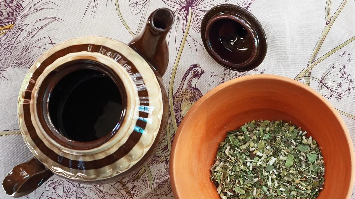 A teapot, a bowl of dried herbs, and a small dish on a tablecloth with a floral pattern.